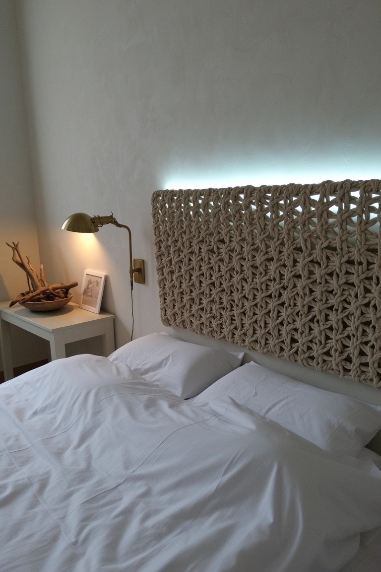 Bedroom with beige woven rope headboard over white bed, brass lamp on side table with driftwood