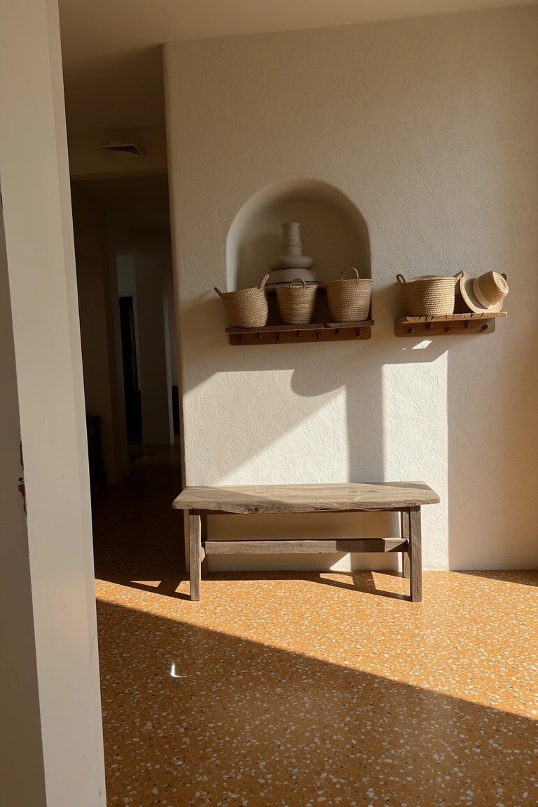 White stucco wall with arched niche holding stacked pottery and woven baskets on wooden shelves, rustic bench below on terracotta floor