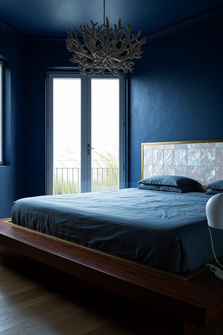 Coastal bedroom with iridescent mother-of-pearl tiled headboard on wooden platform bed, deep blue walls, and balcony view of sea grass