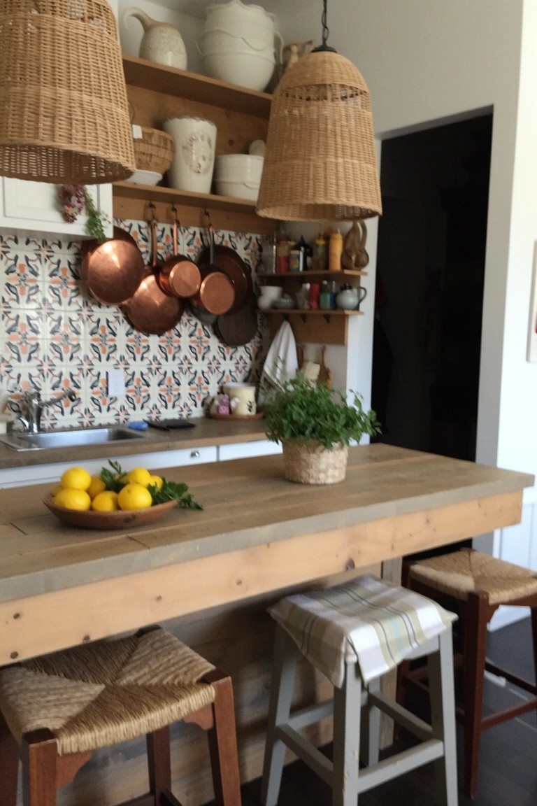 Cozy boho kitchen island with three rattan pendant lights hanging over wooden counter, bar stools, lemons, and herb plant