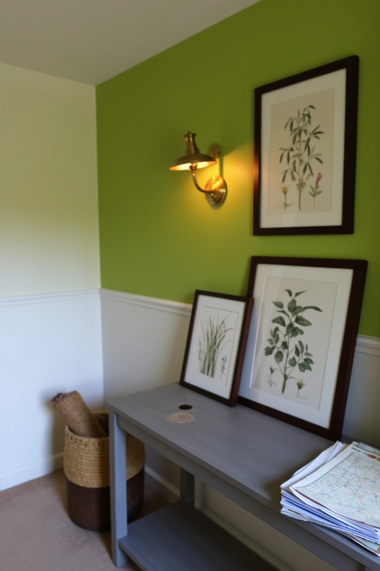 Green upper wall with framed botanical prints above a gray console table holding papers, woven basket storage below, and brass wall sconce lit up