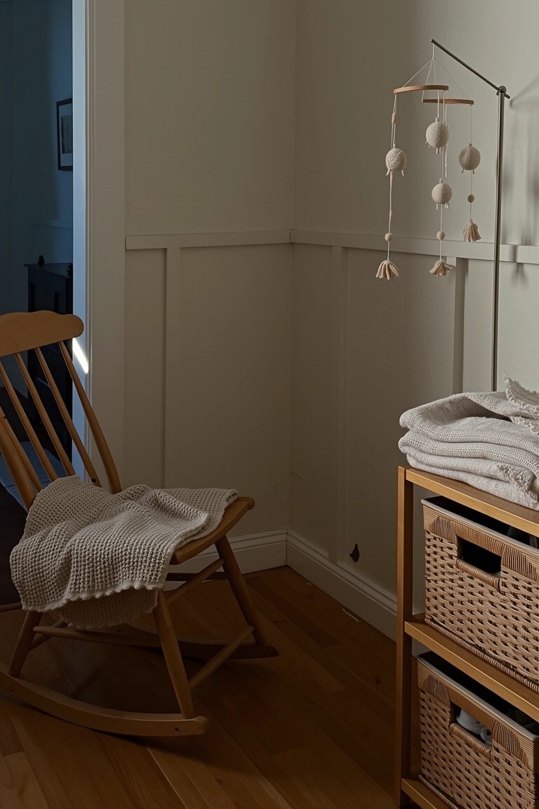 Wooden rocking chair with light gray knit blanket in a neutral nursery corner next to changing table and wicker storage baskets