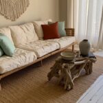 Rattan daybed with white cushions and teal pillows next to driftwood coffee table in light boho room