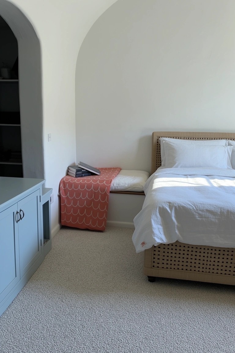 Arched white alcove with built-in bench draped in coral scallop throw, beside rattan bed in light coastal bedroom