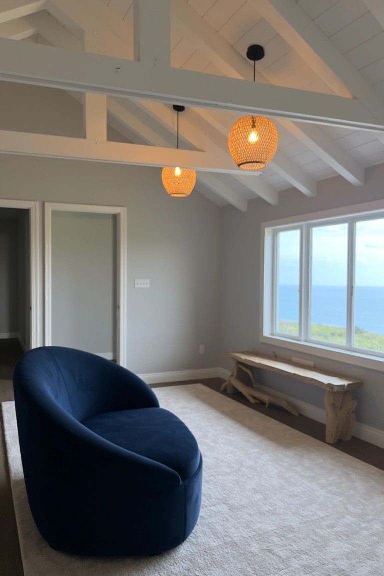 Cozy navy blue curved sofa in a light gray coastal living room with vaulted white ceilings, rattan pendant lights, wooden bench, and ocean view windows