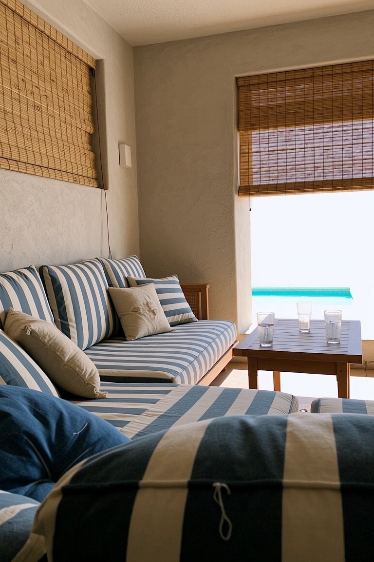 Low blue and white striped sofa with pillows and low table in a light beach room with bamboo blinds