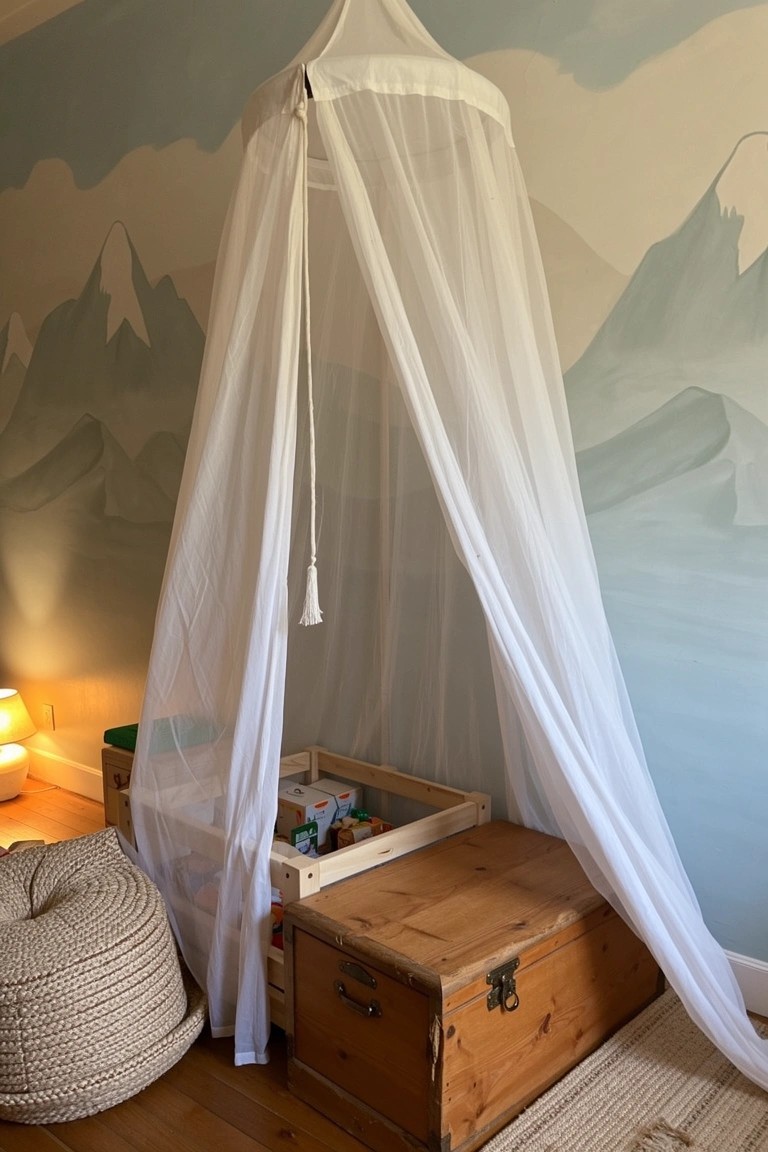 White canopy over wooden storage trunk used as low bed base in kids room with blue mountain mural