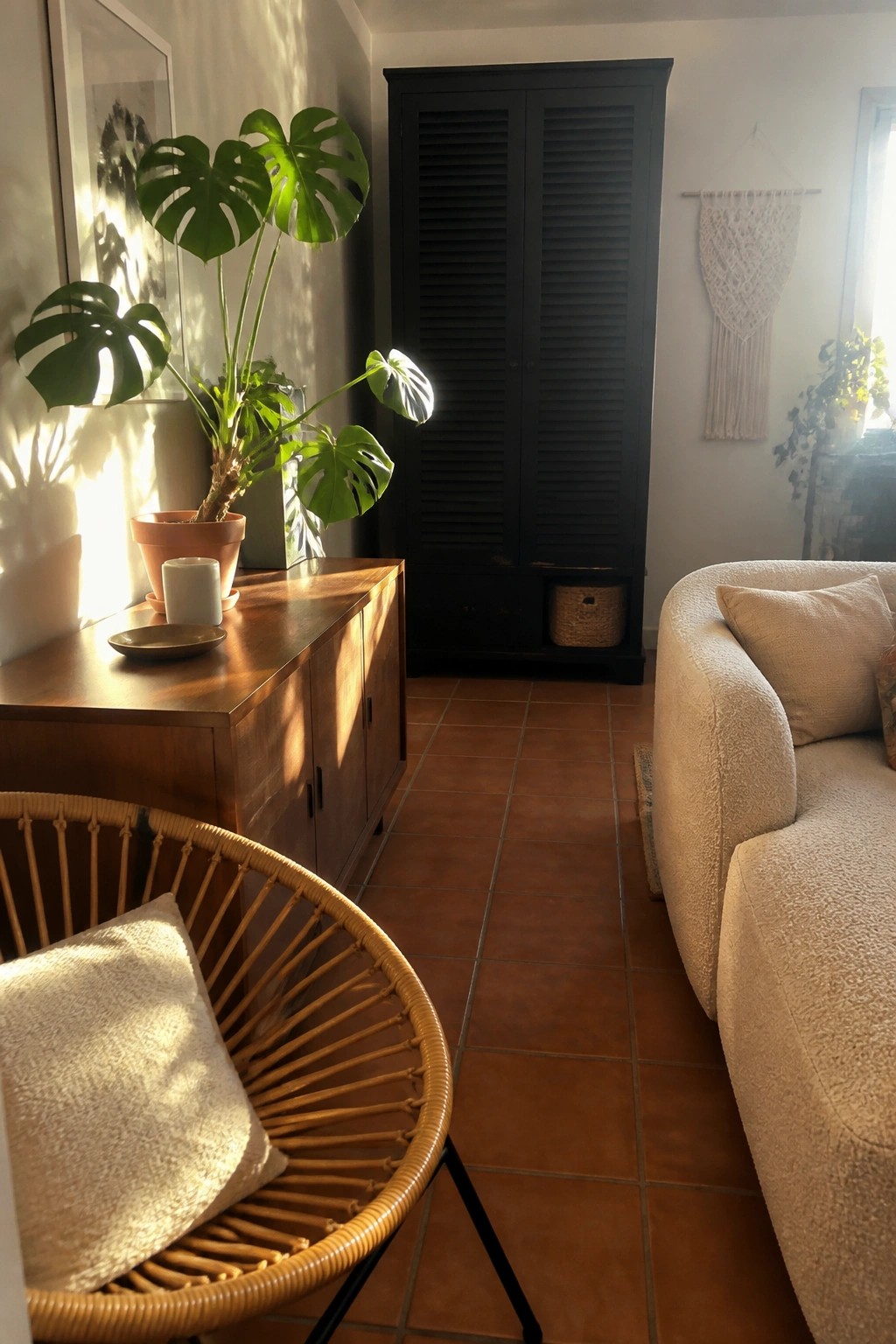 Sunlit room with monstera plant, wooden cabinet, black wardrobe, rattan chair, and sofa.
