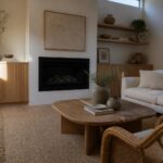 A living room featuring a built-in fireplace with surrounding light wood cabinets and vertical wood slat panels, a white sofa, oval wooden coffee table on a jute rug, and a skylight overhead.