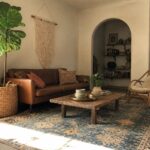Sunlit living room with leather sofa, rustic coffee table, wicker chair, and fiddle leaf fig.