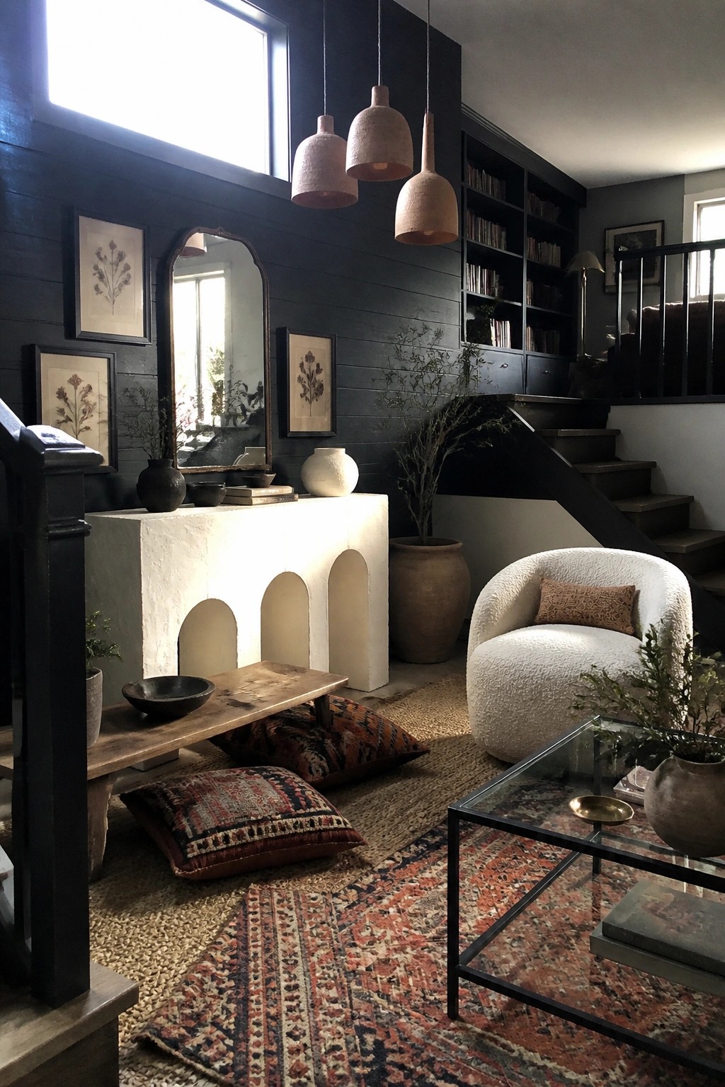 Living room interior with dark charcoal walls, white arched console, layered rugs, white bouclé chair, and hanging pendant lights.