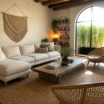 A living room with a low white sectional sofa, wooden coffee table on a jute rug, two woven chairs, a macrame wall hanging, and an arched glass door with sheer curtains.