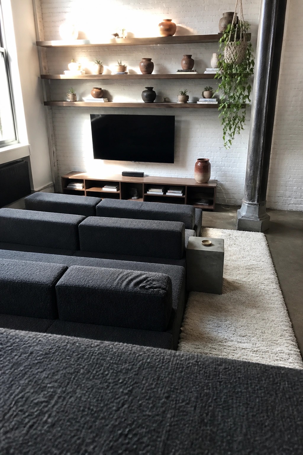 Modern living room with dark gray sectional sofa, floating shelves, and brick wall TV.