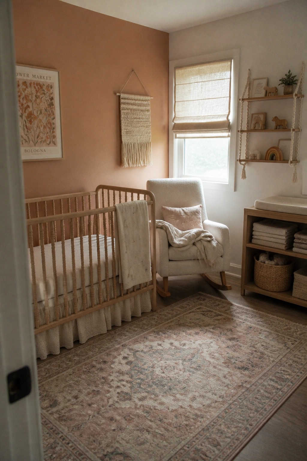 A nursery with peach walls, a light wood crib, a white rocking chair, a macrame wall hanging, and a large patterned rug.