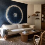 A living room featuring a large blue circular tapestry on the wall above a white sofa and wooden coffee table.