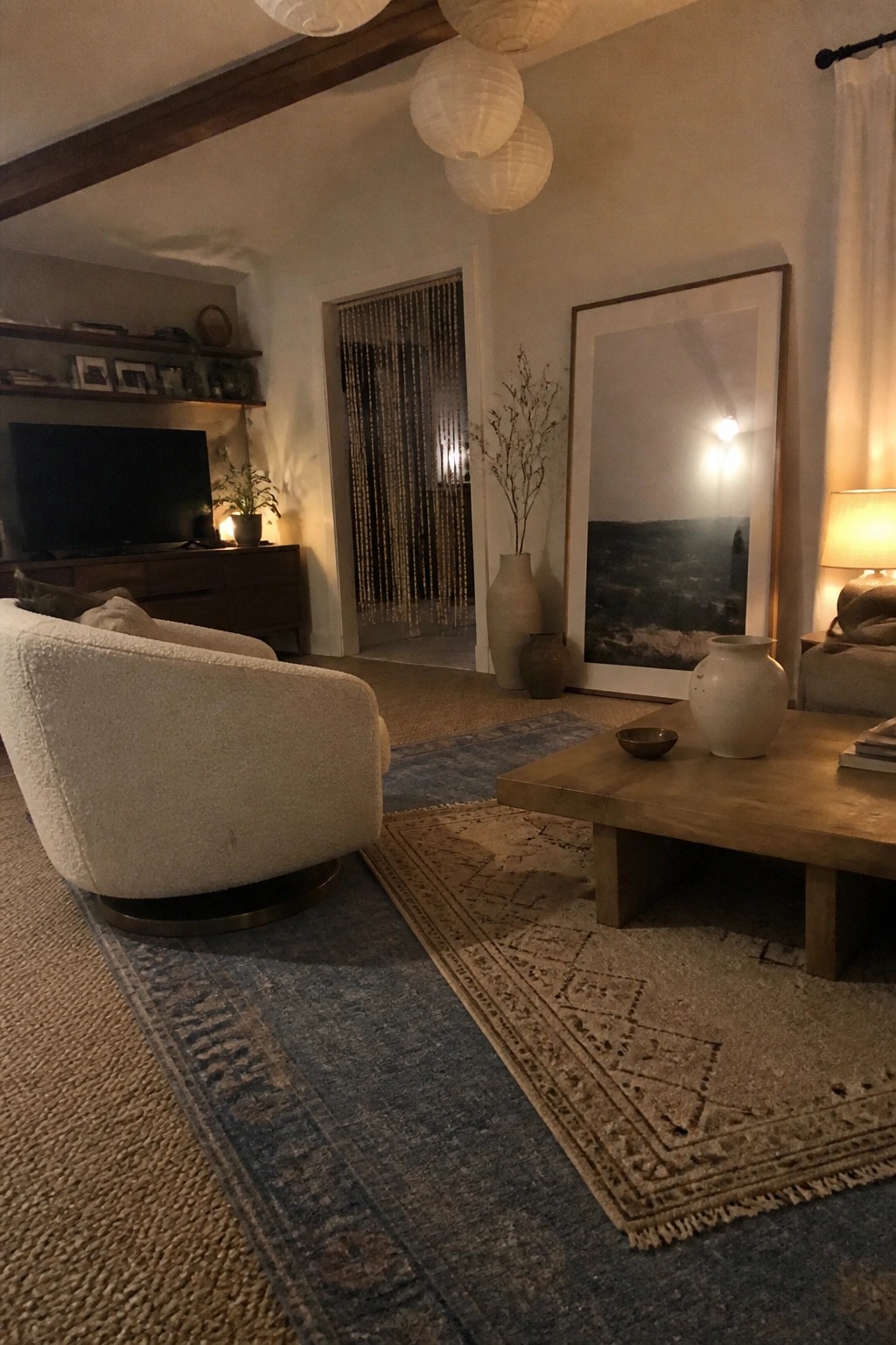 Cozy living room with white boucle armchair, wooden coffee table, layered rugs, and hanging lanterns.