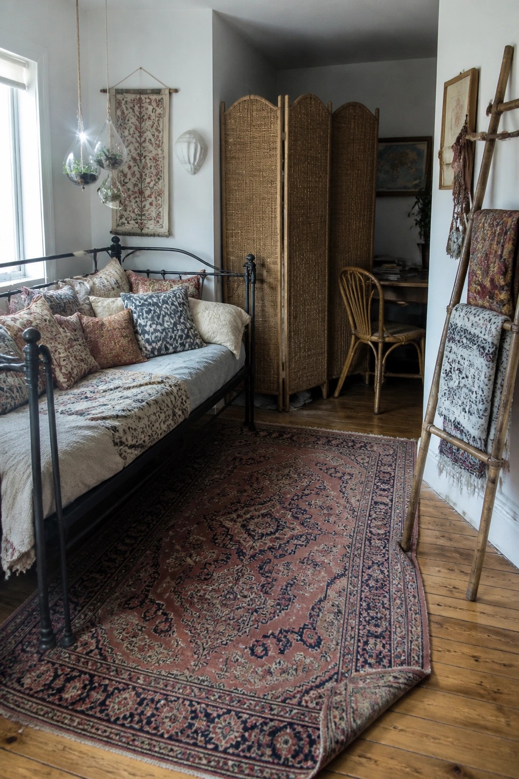 Cozy bohemian bedroom with iron daybed, ornate red rug, rattan screen, and textile ladder.