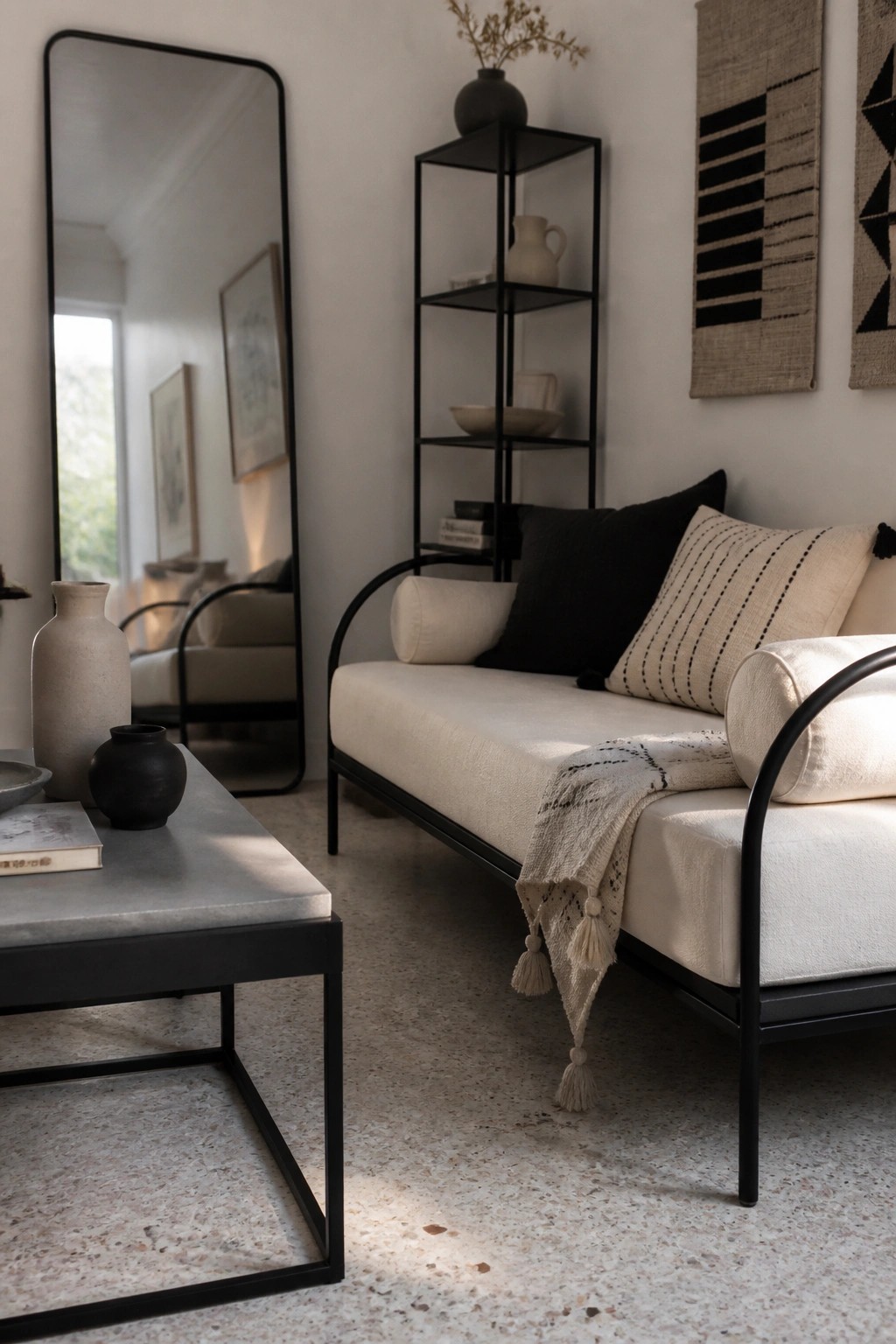 Minimalist living room with white daybed, black metal frame, concrete table, and mirror.