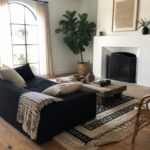 A living room with a dark sofa, white fireplace with black metal screen, wooden coffee table on patterned rugs, and a black floor lamp near an arched window.