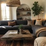 A living room featuring a large dark gray sectional sofa with pillows, a rustic wooden coffee table, and an arched niche with pottery and plants.
