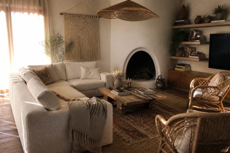 23 Textured Cozy Boho Living Room Ideas Featuring Boucle and Woven Fabrics A living room with a light boucle sofa, woven rattan chairs, a wooden coffee table on layered rugs, and a large woven pendant light near a fireplace.