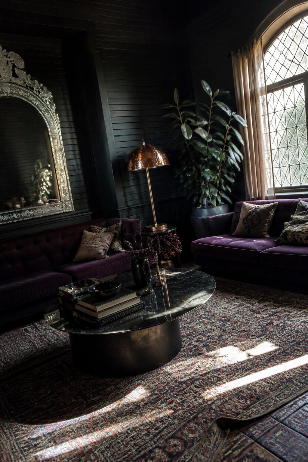 A dark living room featuring purple velvet sofas, a large ornate mirror on the wall, a round coffee table with books, and a patterned rug on the floor.