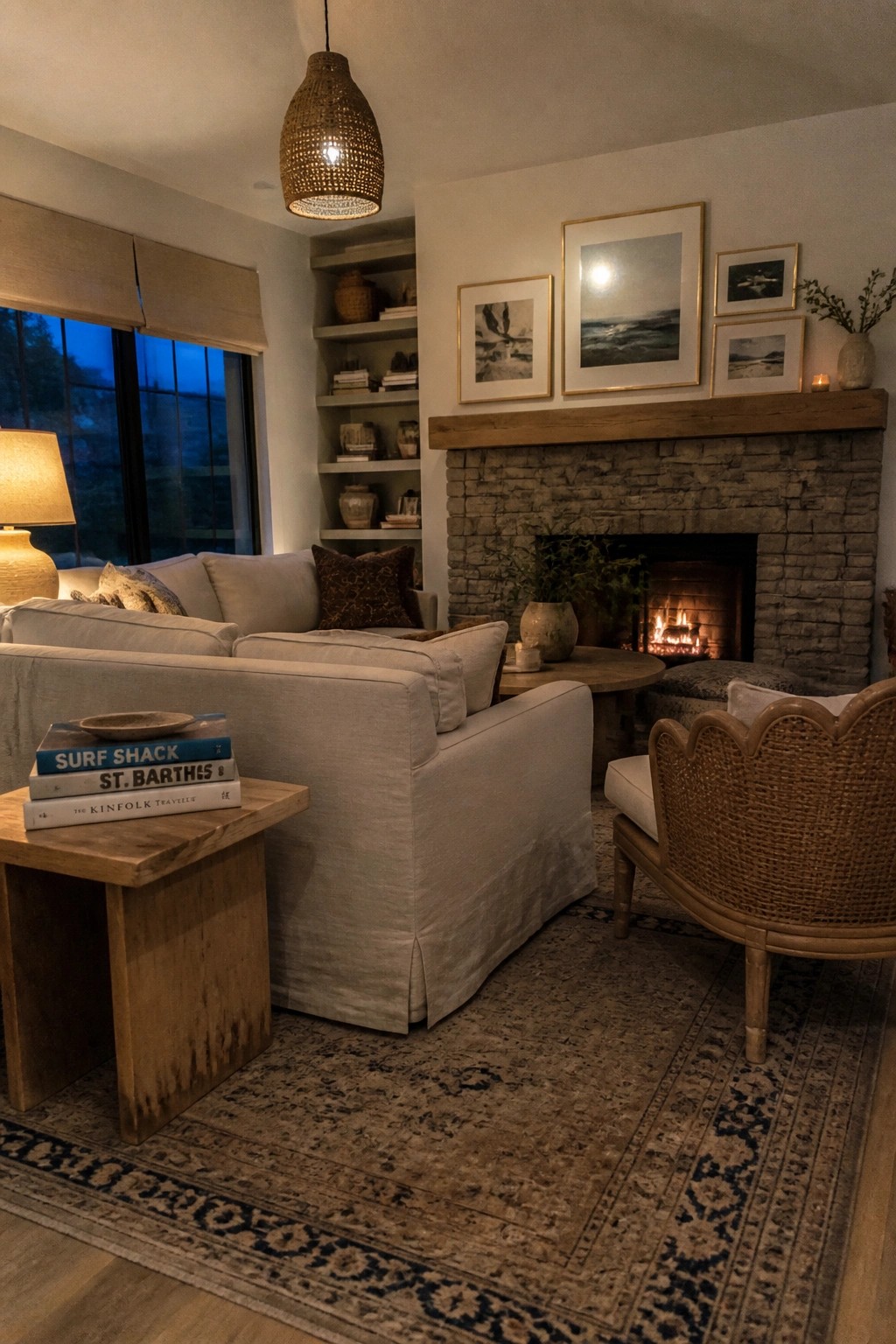 A living room featuring a light linen slipcovered sofa facing a stone fireplace with framed art above the mantel and a woven chair in the foreground.